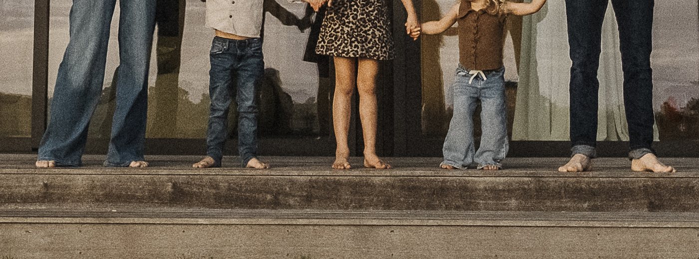 Five pairs of bare feet in a row on a wooden deck: two adults and three children holding hands.